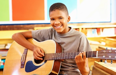 child with a smile holding a
        guitar